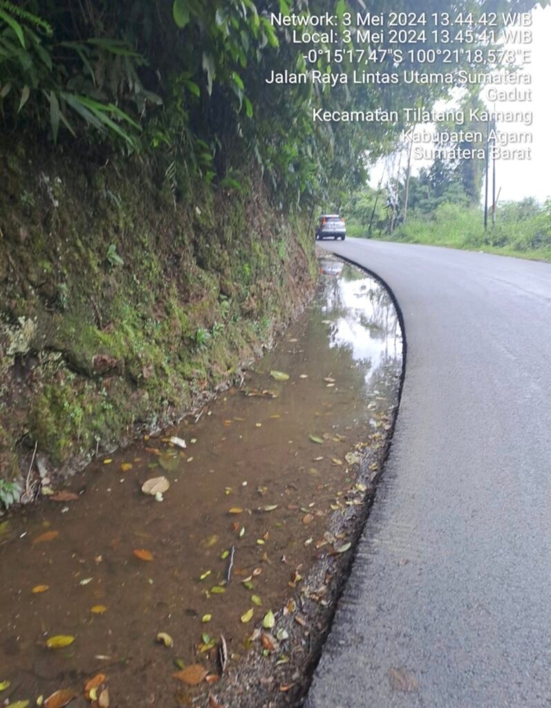 Foto menunjukkan jalan dengan genangan air di tepinya, yang disebabkan oleh tidak adanya saluran air.